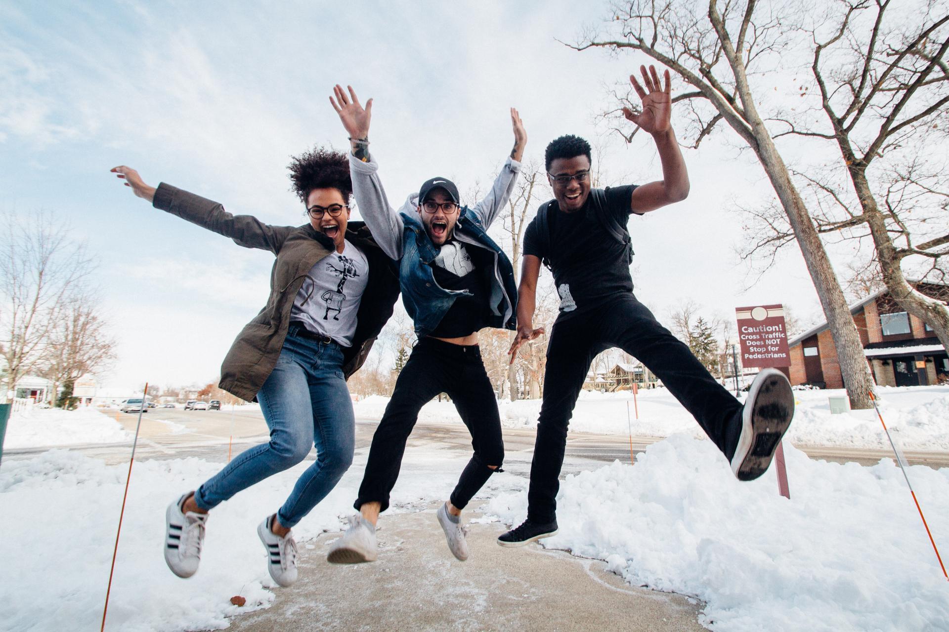three students jumping and laughing on a snowy sidewalk