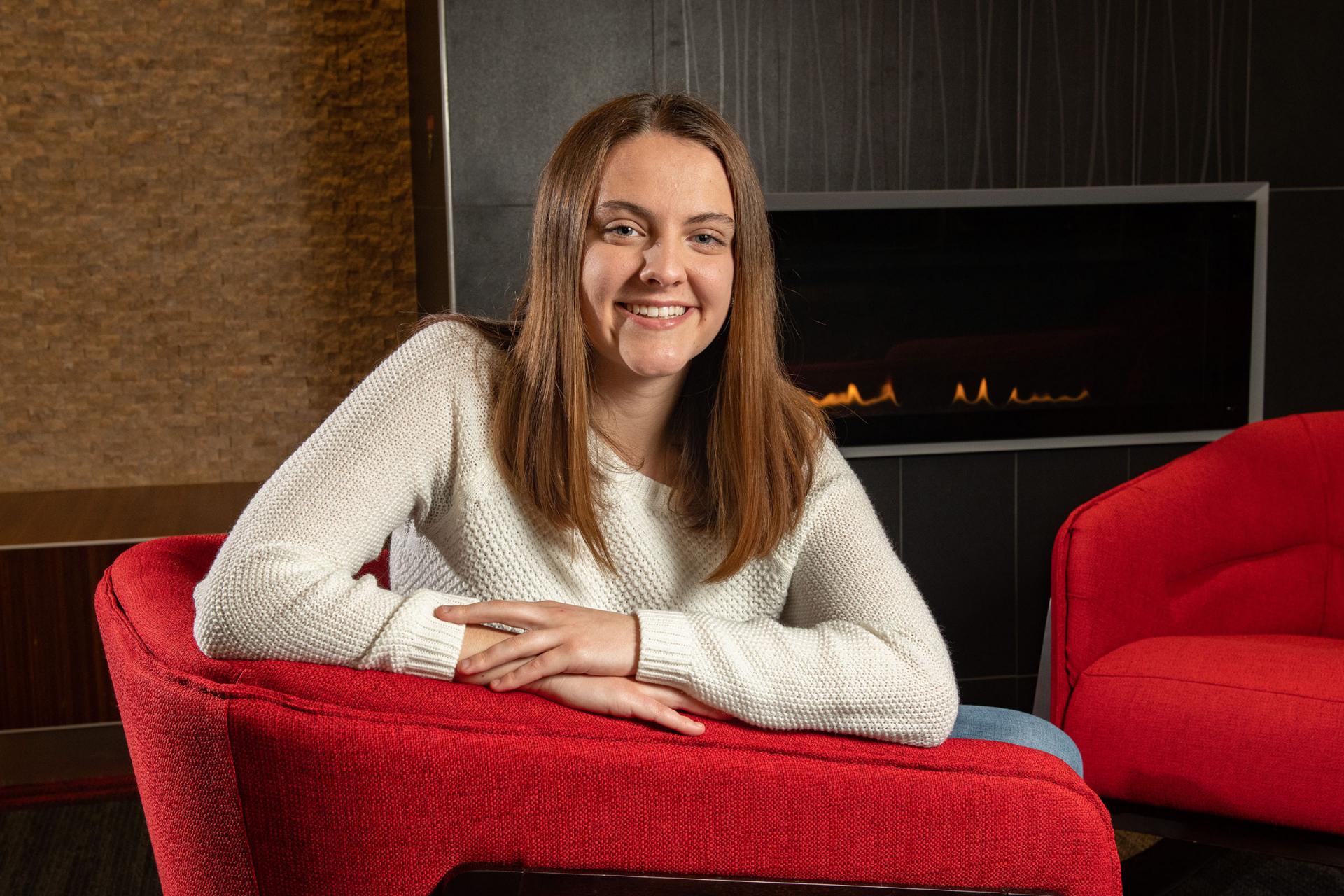 Abby Seibel sitting in red chair by fireplace