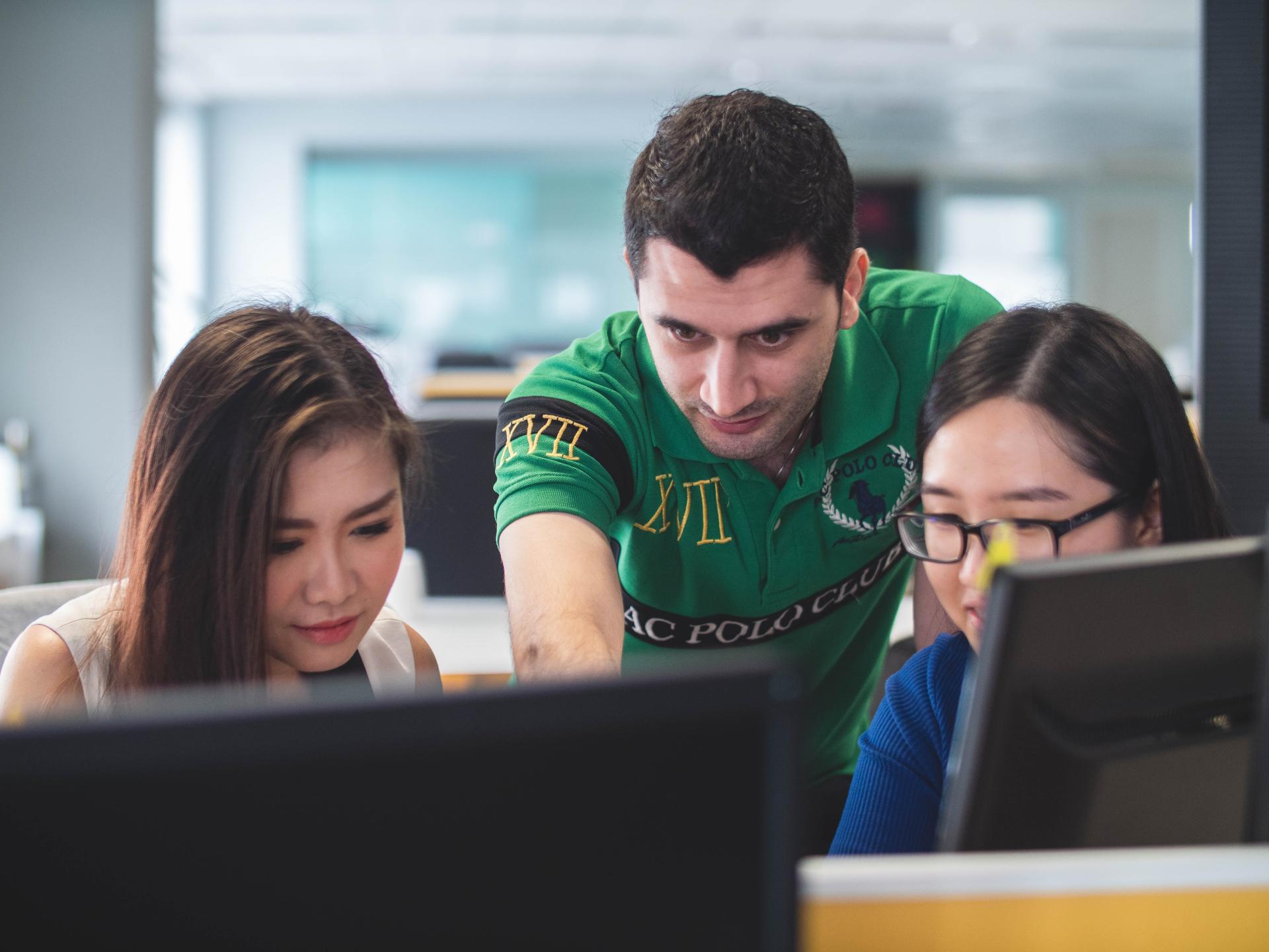 Students working on computer, individual helping them 