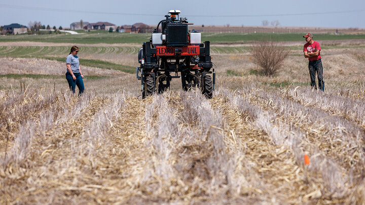 A man and a woman walk behind the Flex-Ro autonomous planting robot in a field.