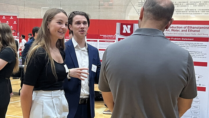 A young woman and young man present their research project poster to a man.