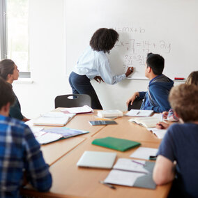 Female High School Tutor At Whiteboard Teaching Maths Class
