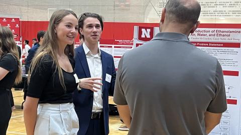 Chemical engineering students Amanda Goertzen (left) and Jackson Young discuss their project with a visitor during the 2023 College of Engineering Senior Design Showcase at the Coliseum. The team designed a process to reduce carbon emissions and more sustainably produce ethanolamines — compounds widely used in cleaning agents, cosmetics and pharmaceuticals.
