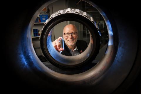 Joe Turner holds a 3D printed railcar bearing. He is photographed through an actual bearing and housing that fits on the end of each axle of a railcar axle.